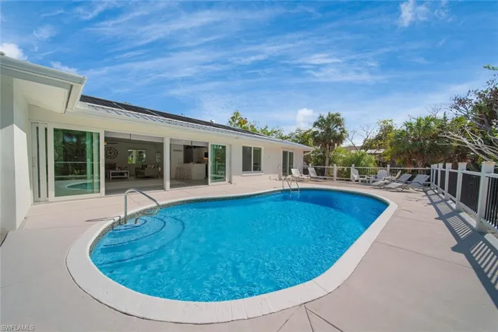 In-ground pool with integrated steps, expansive concrete patio, multi-panel sliding glass doors, and perimeter fencing