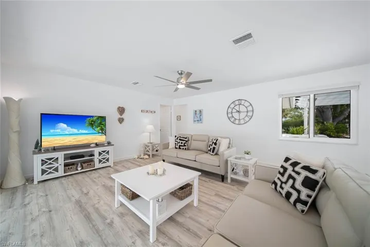 Living area featuring wood-finish flooring, a neutral color palette, a central ceiling fan with integrated lighting, and a single-pane window