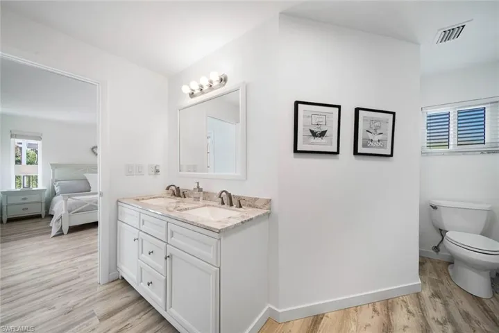 Double vanity featuring white cabinetry, stone-finish countertops, dual under-mount sinks, and wall-mounted light fixtures with glass shades
