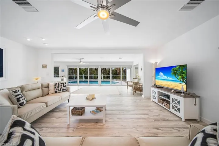 Living area featuring wood-finish flooring, recessed lighting, a brushed metal ceiling fan, and floor-to-ceiling glass sliding doors opening to a swimming pool