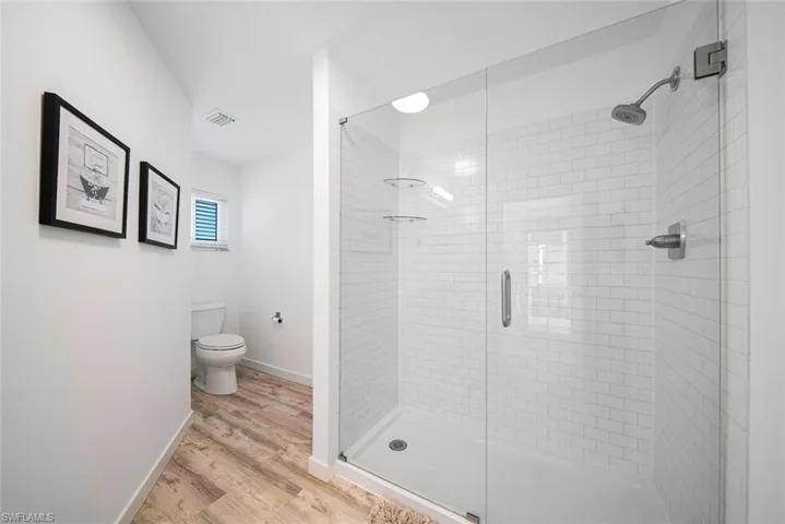 Walk-in shower featuring a glass enclosure, white subway tile surround, integrated shelving, and metal shower hardware, paired with wood-finish flooring and a standard-height toilet