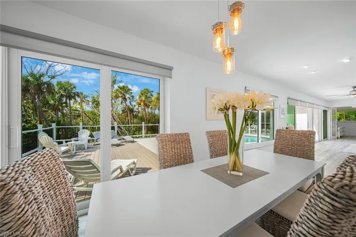 Dining area featuring wood-finish flooring, recessed lighting, and a multi-pendant light fixture, opening to an expansive deck with composite decking and white railing