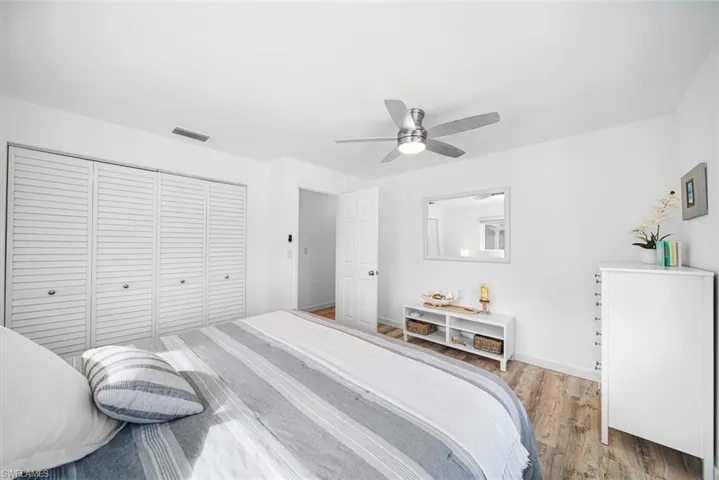 Wood-finish flooring, white louvered closet doors, and brushed metal ceiling fan with integrated lighting