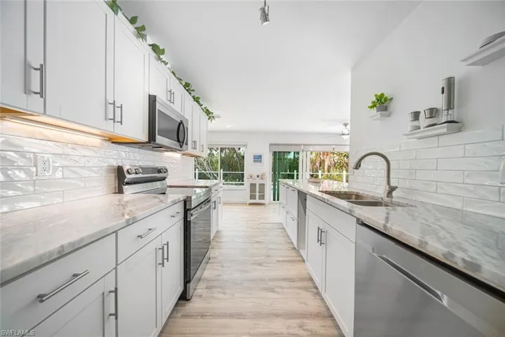 Kitchen featuring white cabinetry, stone-finish countertops, stainless steel appliances, subway tile backsplash, and wood-finish flooring