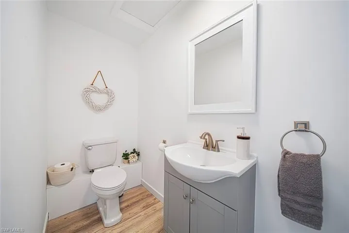 Bathroom featuring a vanity with a white integrated basin, metallic faucet, grey shaker-style cabinetry, a wall-mounted mirror with a white frame, and wood-finish flooring
