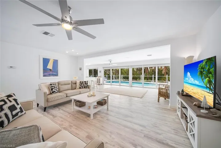 Living area featuring wood-finish flooring, a multi-blade ceiling fan, and sliding glass wall panels opening to a screened-in swimming pool