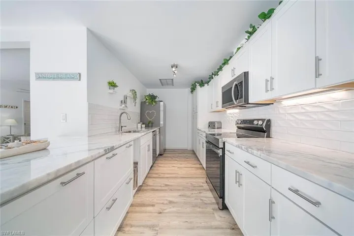 Kitchen featuring white shaker-style cabinetry, stone-surface countertops, textured tile backsplash, stainless steel appliances, and wood-finish flooring