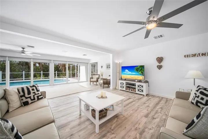 Living area featuring wood-finish flooring, recessed lighting, and dual ceiling fans, highlighting floor-to-ceiling glass sliding doors with access to an exterior swimming pool