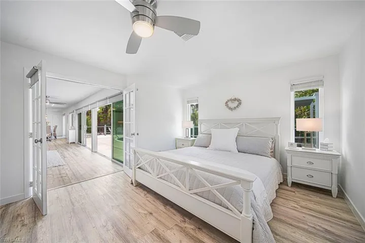Light-filled room featuring wood-finish flooring, double French doors, large windows, and a brushed nickel ceiling fan