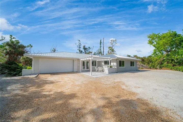 Single-story exterior featuring a light-toned metal roof, attached two-car garage, white pergola, and gravel driveway
