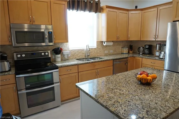 Kitchen with appliances with stainless steel finishes, tasteful backsplash, light stone countertops, and wood cabinets