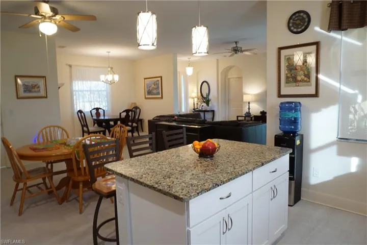 Kitchen with a ceiling fan, wood cabinets, light stone countertops, a kitchen breakfast bar, and open floor plan