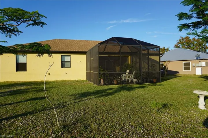 Rear view of house featuring a yard, a lanai, a sunroom, roof with shingles, and stucco siding