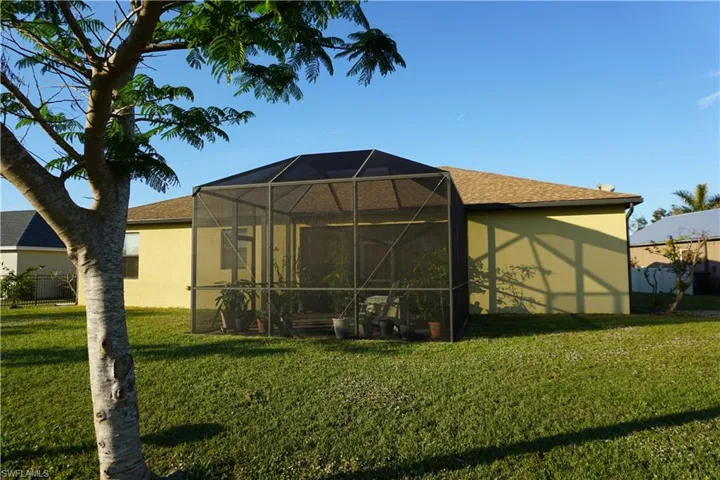 Back of property with a yard, a screened lanai, stucco siding, and a shingled roof