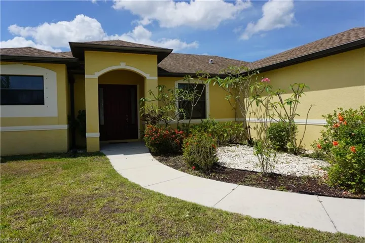 Property entrance featuring a lawn, stucco siding, and a shingled roof