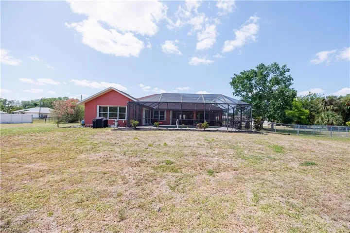Back of house with a lawn, glass enclosure, and fence