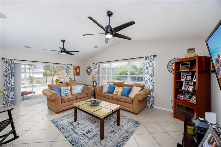 Living area featuring light tile patterned floors, ceiling fan, vaulted ceiling, and baseboards