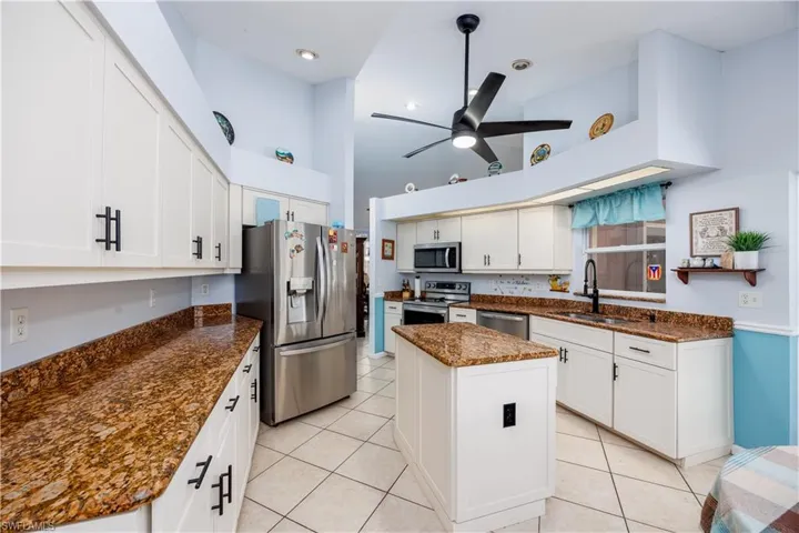 Kitchen featuring appliances with stainless steel finishes, a kitchen island, a sink, a high ceiling, and light tile patterned flooring