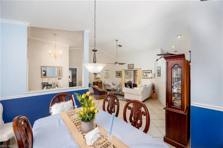 Tiled dining room with visible vents, ceiling fan with notable chandelier, crown molding, and vaulted ceiling