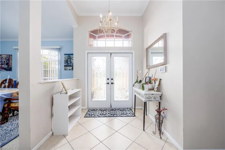 Entrance foyer featuring baseboards, an inviting chandelier, ornamental molding, french doors, and tile patterned flooring