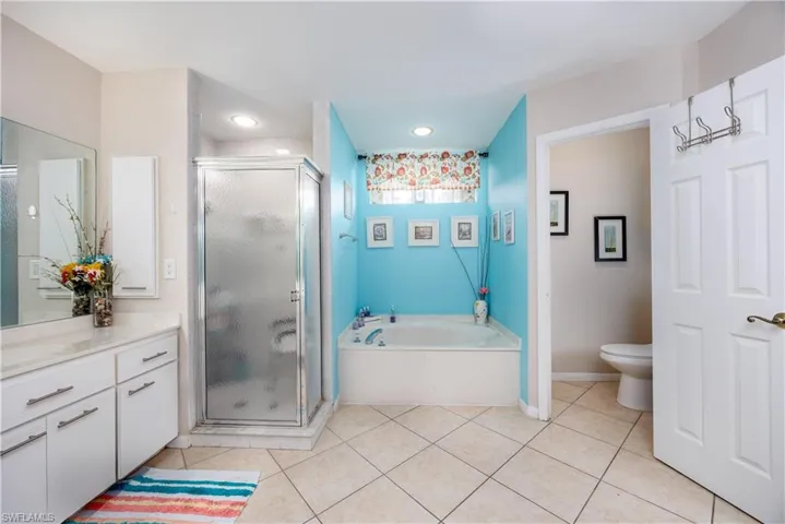 Bathroom featuring a stall shower, toilet, tile patterned floors, a garden tub, and vanity