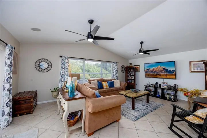 Living room featuring light tile patterned flooring, ceiling fan, and vaulted ceiling