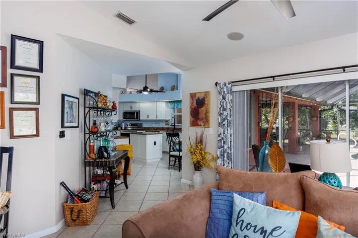 Living room featuring light tile patterned flooring, ceiling fan, visible vents, vaulted ceiling, and baseboards