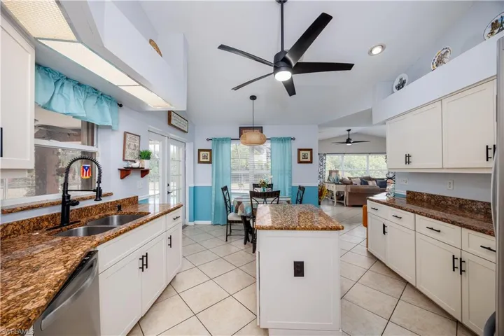Kitchen featuring stainless steel dishwasher, a kitchen island, vaulted ceiling, ceiling fan, and a sink