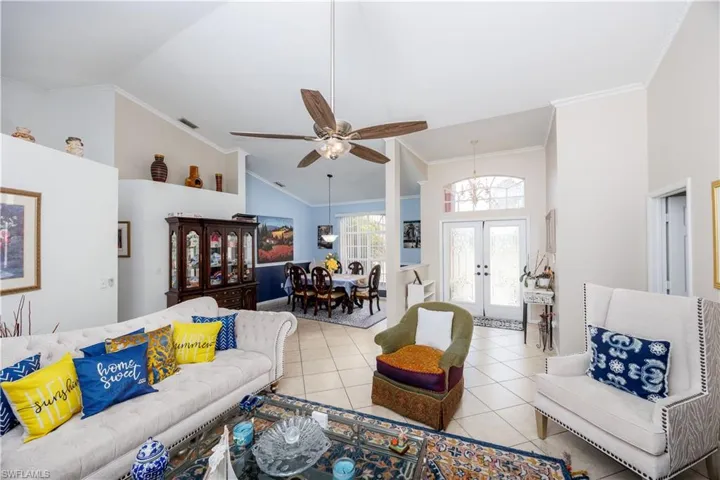 Tiled living area with french doors, a ceiling fan, high vaulted ceiling, and crown molding