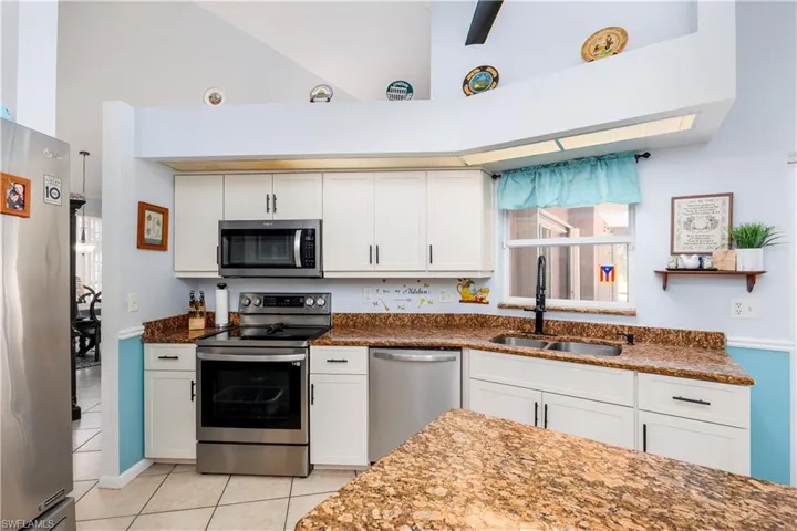 Kitchen with high vaulted ceiling, stainless steel appliances, light tile patterned floors, and a sink