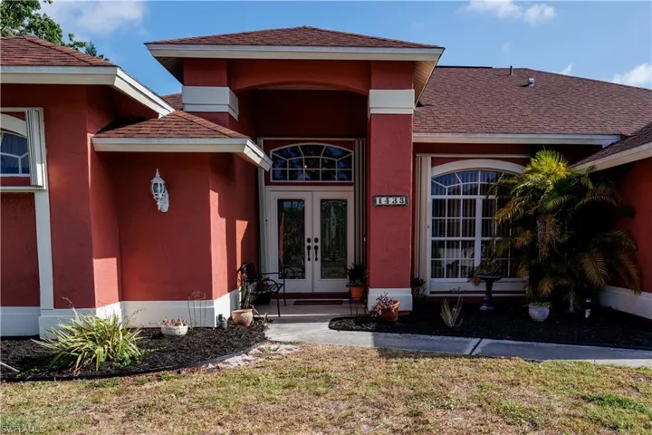 Doorway to property featuring stucco siding, roof with shingles, a yard, and french doors