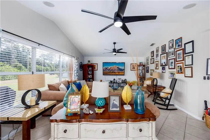 Living area featuring light tile patterned floors, ceiling fan, vaulted ceiling, and baseboards