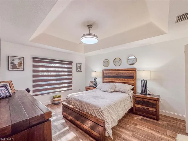 Bedroom featuring a raised ceiling, wood finished floors, baseboards, and visible vents