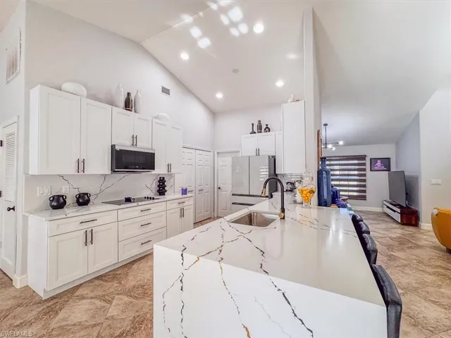 Kitchen featuring black electric cooktop, stainless steel microwave, a sink, freestanding refrigerator, and white cabinets