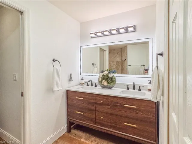 Full bathroom featuring double vanity, wood finished floors, baseboards, and a sink