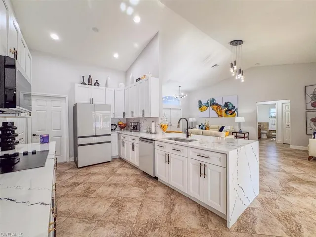Kitchen featuring a peninsula, appliances with stainless steel finishes, a sink, open floor plan, and an inviting chandelier