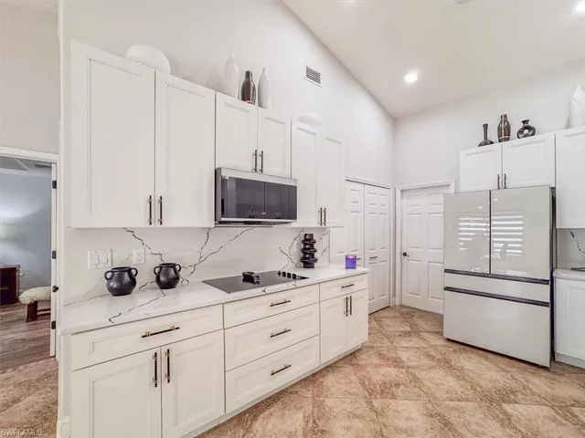 Kitchen featuring white cabinetry, black electric cooktop, visible vents, and freestanding refrigerator