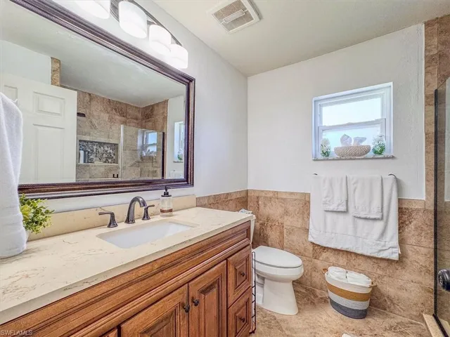 Bathroom featuring tile walls, vanity, visible vents, and a shower stall