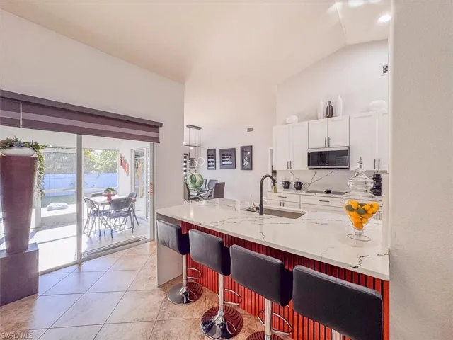 Kitchen with tasteful backsplash, stainless steel microwave, a sink, white cabinets, and light stone countertops