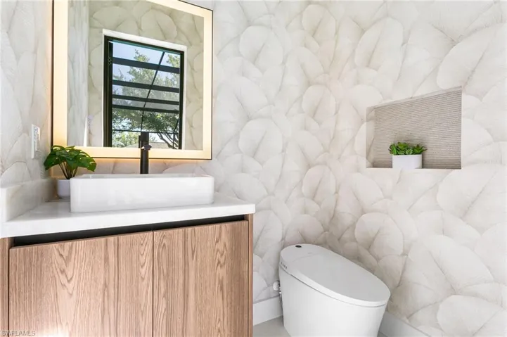 Pool bathroom with electric toilet with bidet functions, lighted mirror, vessel sink, quartzite countertop, and Italian wallpaper walls and handcrafted Italian embroided wallpaper accent!
