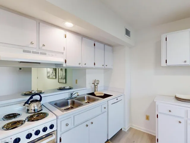 Kitchen with white cabinetry, sink, white appliances, and light wood-type flooring