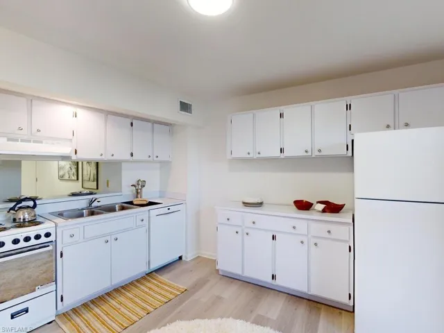 Kitchen with white cabinets, light wood-type flooring, and white appliances