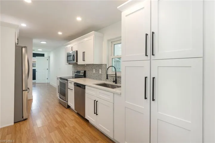 White shaker cabinetry with matte black hardware, stainless steel appliances, stone countertops, and a patterned tile backsplash