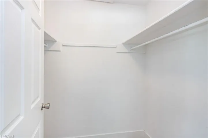 White door with brushed nickel hardware opens to a bright closet featuring white shelving and a hanging rod