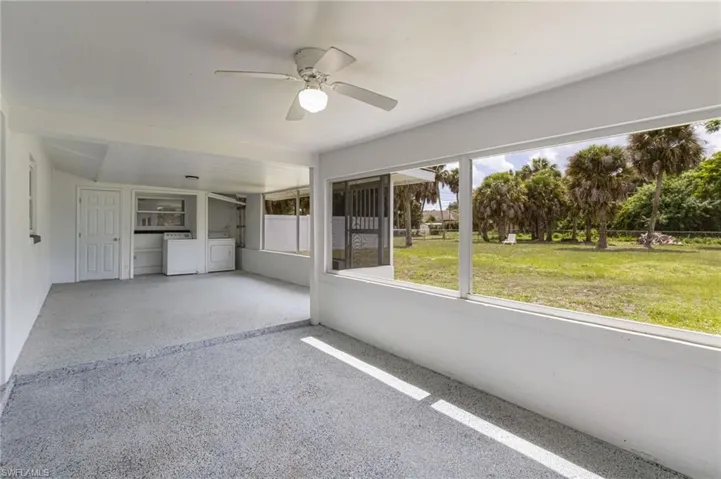 Screened-in patio with textured gray flooring, ceiling fan, and expansive views of the green landscape and palm trees
