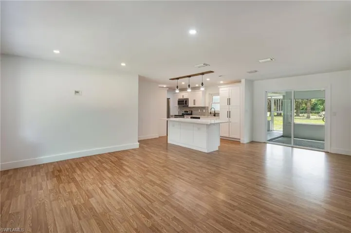 Bright open-concept interior featuring wood-finish flooring, recessed lighting, a kitchen island with seating, a modern pendant light fixture, and sliding glass doors to the exterior