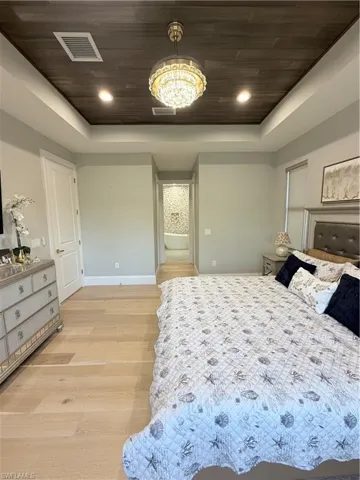 Bedroom featuring light wood-type flooring, wood ceiling, a raised ceiling, recessed lighting, and ensuite bathroom