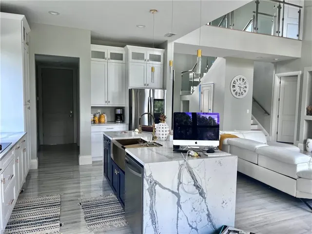 Kitchen with white cabinets, open floor plan, light stone countertops, appliances with stainless steel finishes, and hanging light fixtures