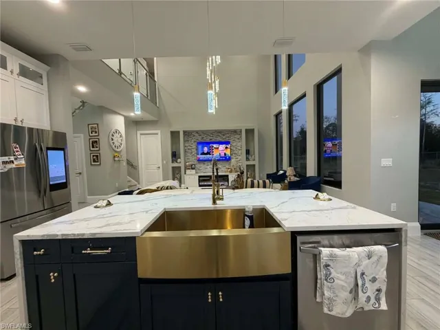 Kitchen with light stone countertops, stainless steel appliances, light wood-style flooring, hanging light fixtures, and dark cabinets