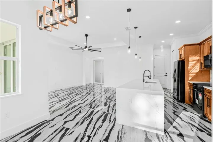 Kitchen featuring decorative light fixtures, black appliances, recessed lighting, brown cabinets, and a center island with sink